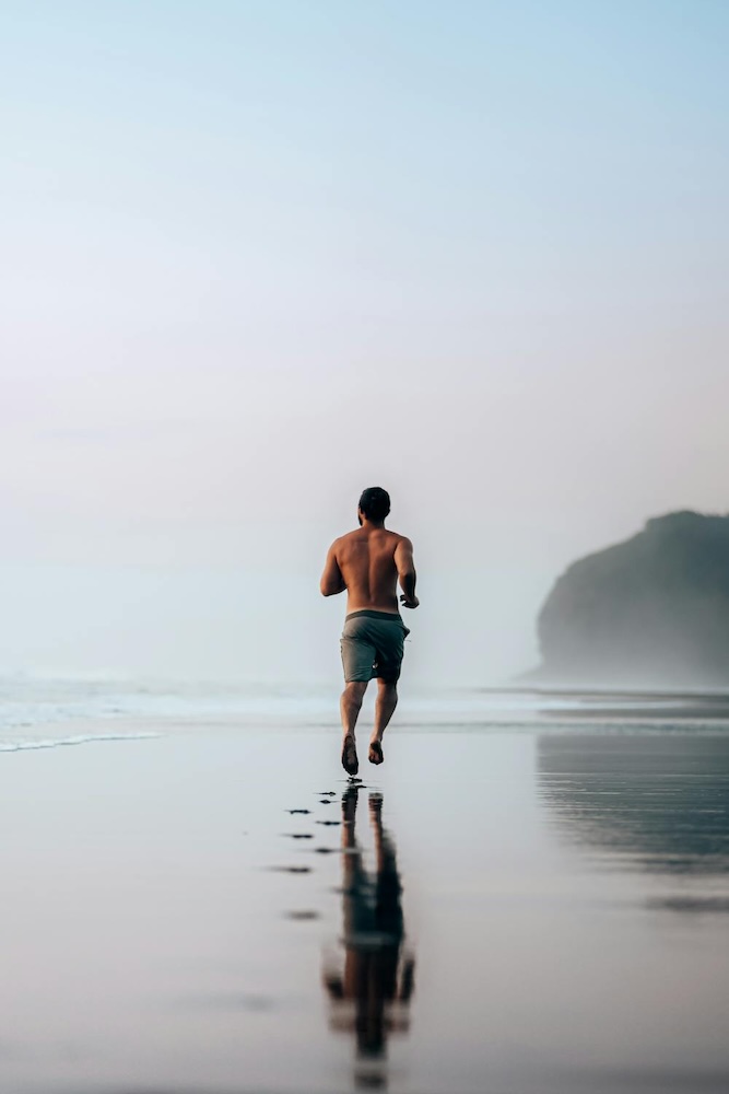 Ein energiegeladener Athlet joggt am Strand entlang, voller Vitalität. Die unterstützende IV-Infusion stärkt seine Ausdauer und unterstützt eine schnelle Regeneration – perfekt für Spitzenleistung und Erholung.
