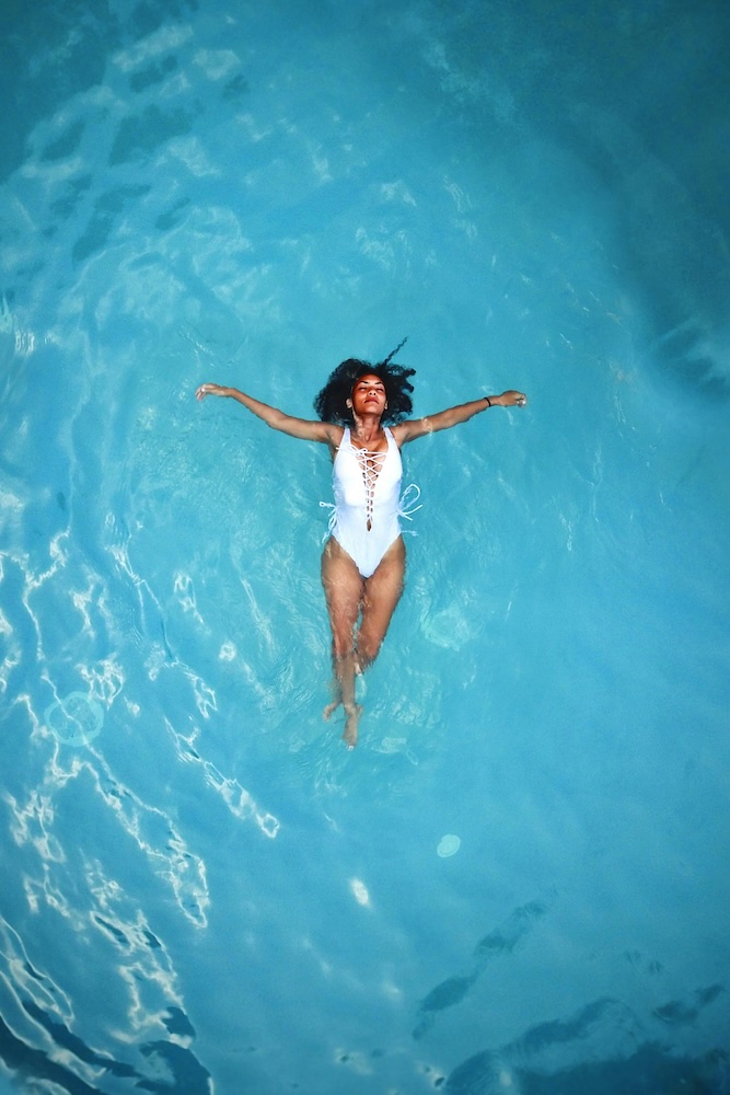 Eine entspannte Frau badet in klarem, blauem Wasser – ein Sinnbild für Erfrischung und Regeneration. Die Beauty IV Drip Therapie liefert essenzielle Vitamine für strahlende Haut und natürliche Schönheit von innen.